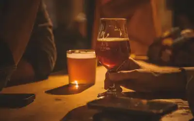 Mão segura taça tulipa de cerveja âmbar-avermelhada em mesa de bar