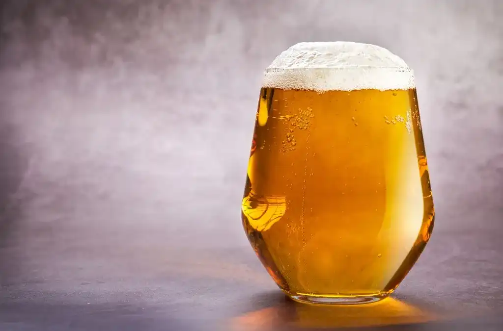 Copo tulipa com cerveja dourada clara, efervescente e espuma branca densa