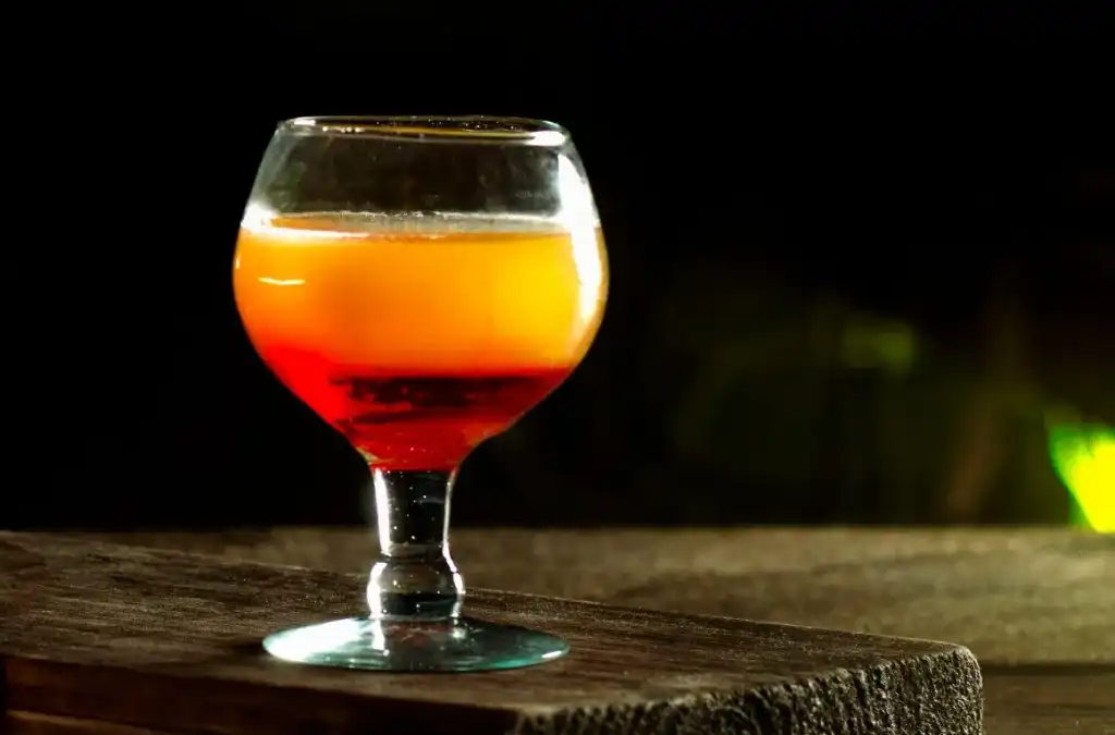 Cálice baixo com cerveja de tons rubi e dourado sobre tábua de madeira