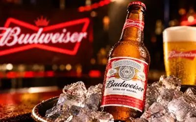 Garrafa de Budweiser gelada sobre gelo, com copo da marca e letreiro vermelho ao fundo