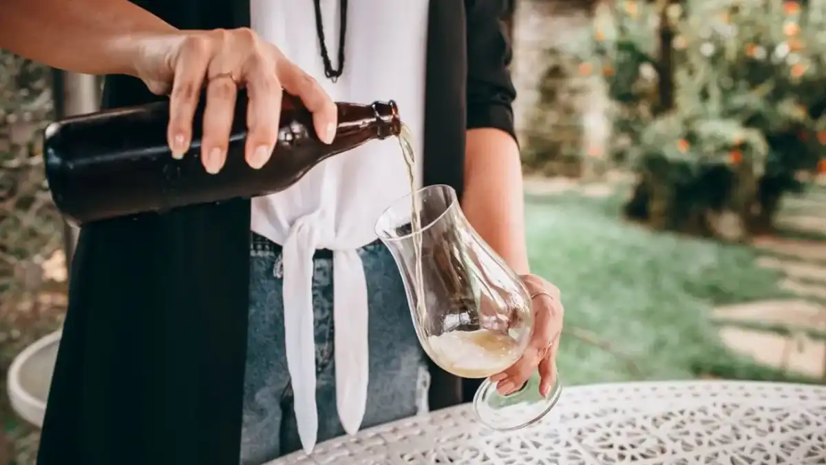 Pessoa servindo cerveja clara de garrafa em taça tulipa ao ar livre
