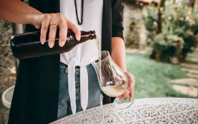 Pessoa servindo cerveja clara de garrafa em taça tulipa ao ar livre