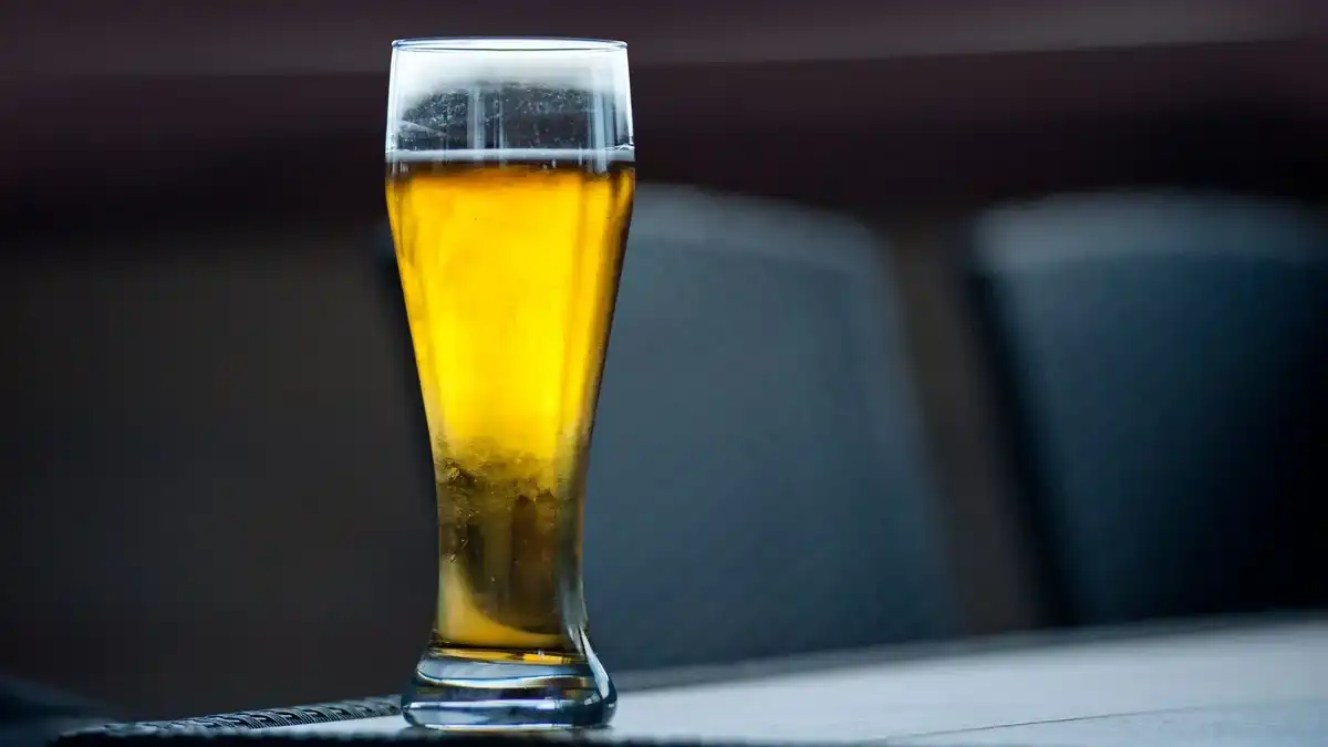 Copo alto de cerveja Golden Ale dourada cristalina com fina espuma branca e condensação, sobre mesa escura