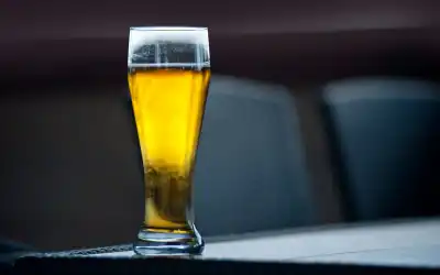 Copo alto de cerveja Golden Ale dourada cristalina com fina espuma branca e condensação, sobre mesa escura