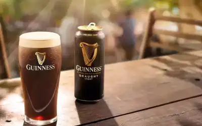 Copo e lata de Guinness Draught em mesa de madeira ao sol
