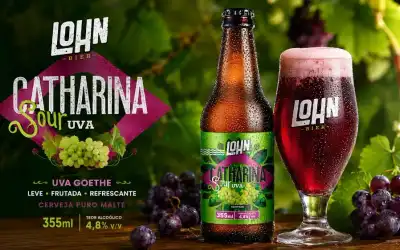 Garrafa e taça Lohn Bier Catharina Sour Uva Goethe sobre mesa com uvas, vinhedo ao fundo