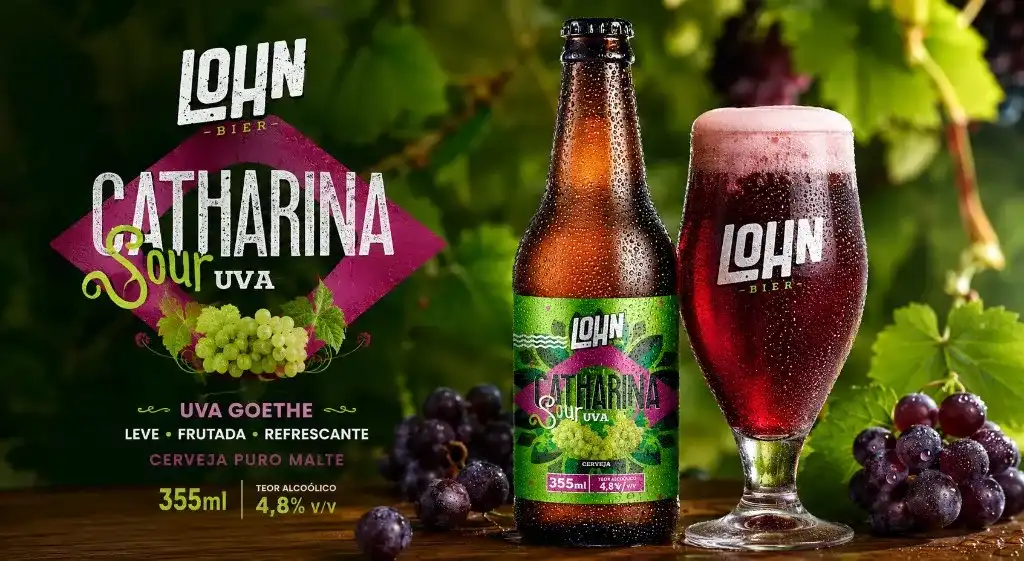 Garrafa e taça Lohn Bier Catharina Sour Uva Goethe sobre mesa com uvas, vinhedo ao fundo