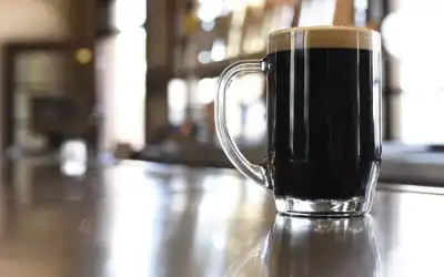 Caneca de cerveja preta com colarinho cremoso sobre balcão reflexivo