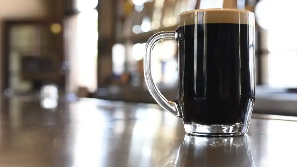Caneca de cerveja preta com colarinho cremoso sobre balcão reflexivo
