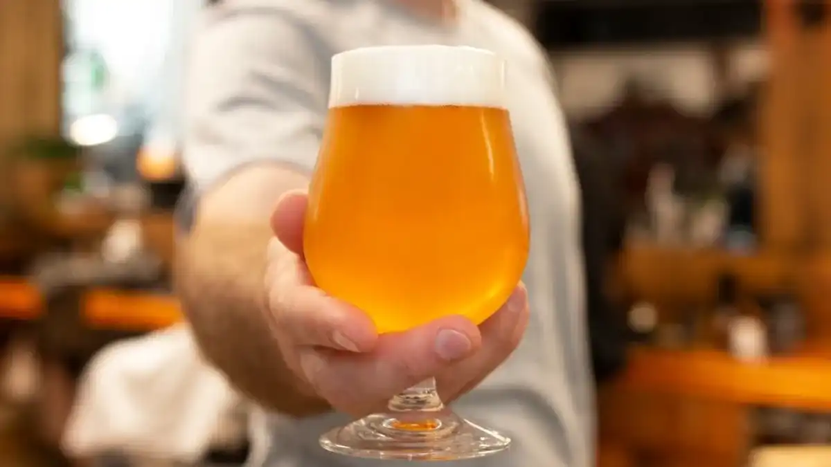 Mão segurando taça tulipa com cerveja dourada e espuma cremosa