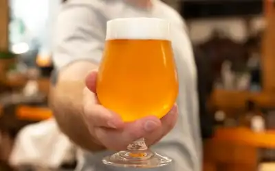 Mão segurando taça tulipa com cerveja dourada e espuma cremosa