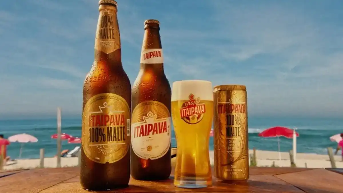 Garrafas, lata e copo de Itaipava 100% Malte e Pilsen em mesa de madeira na praia