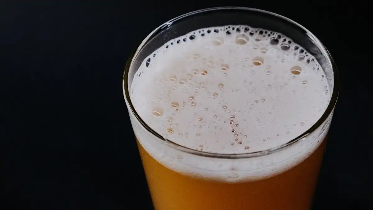 Copo alto de cerveja Weiss turva e dourada com espuma branca cremosa