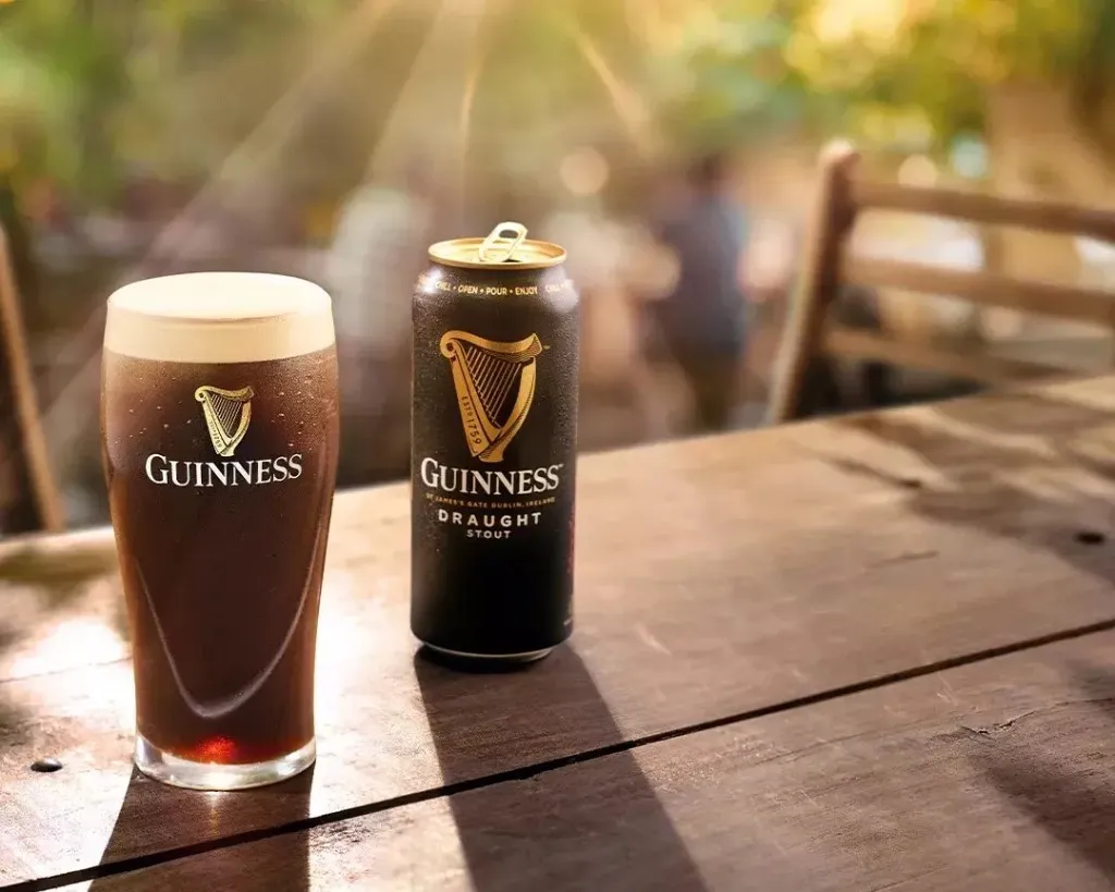 Copo e lata de Guinness Draught em mesa de madeira ao sol